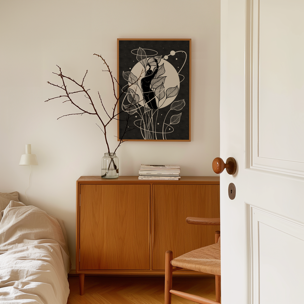 A framed black and white art print featuring a minimalist feminine figure beneath a full moon hangs on a white wall above a mid century modern wooden sideboard in a serene bedroom. Inspired by the menstrual cycle and the lunar cycle, this self love artwork celebrates feminine wisdom, inner balance, and the natural rhythms of the body, creating a calming and meaningful focal point.
