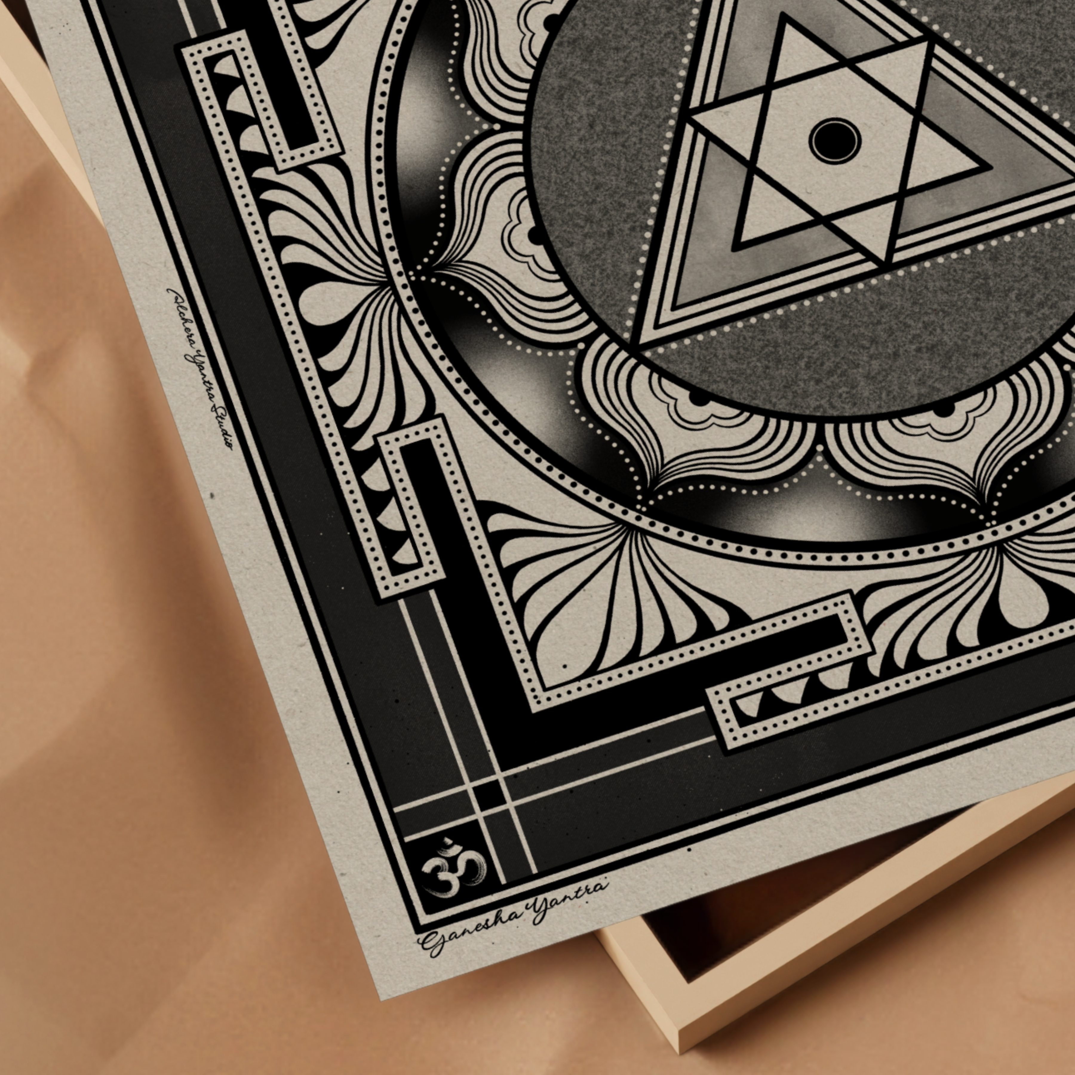 A square Ganesha yantra art print with a black and gray sacred geometric mandala design, styled on a light wood tray over a beige background. The print features the text 'Ganesha yantra' and an Om symbol.