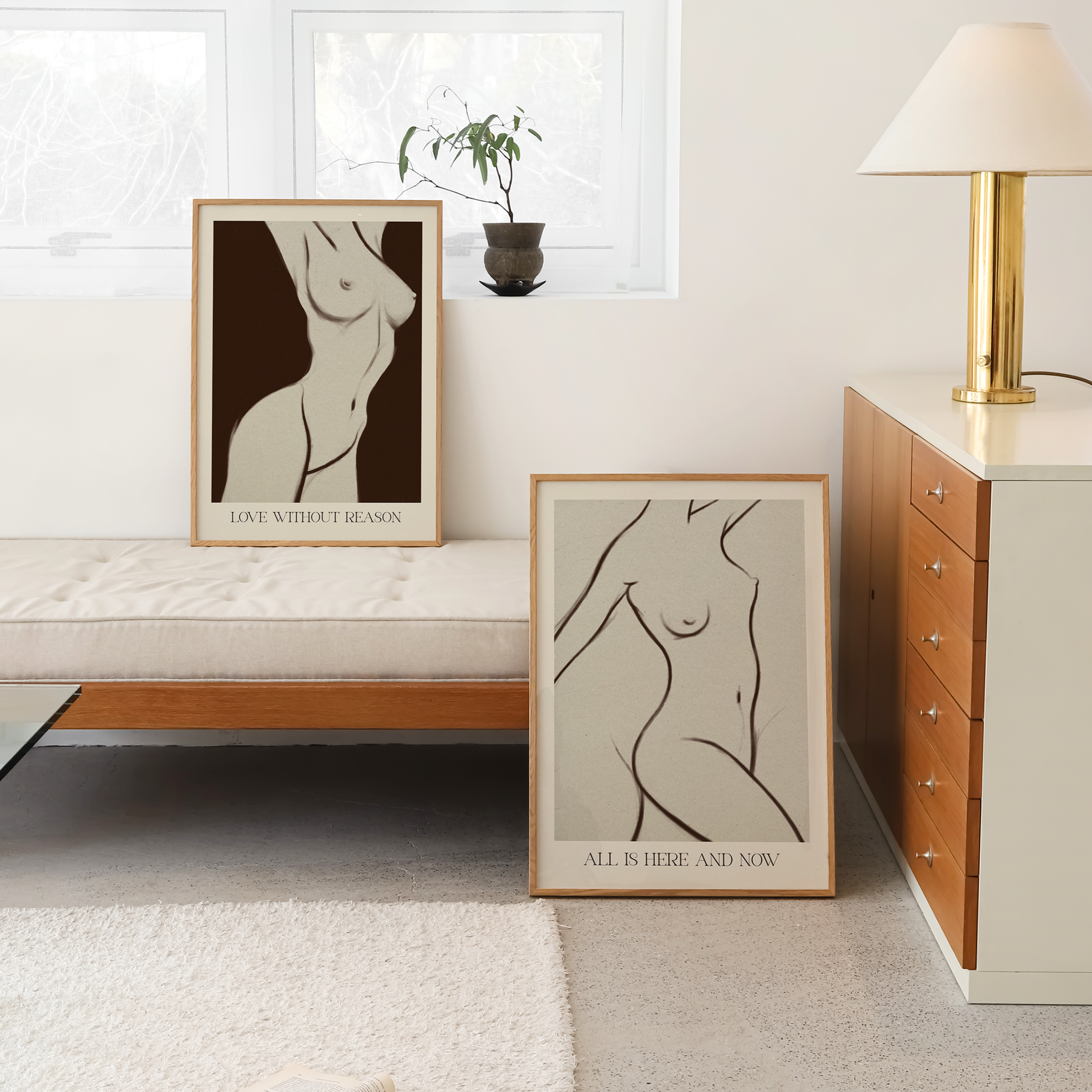 Two framed abstract affirmation art prints featuring minimalist line drawings of female nudes are displayed in a modern, sunlit room. One print is propped up on a white bench, and the other lies on the floor next to a mid-century modern wooden cabinet and a gold lamp.