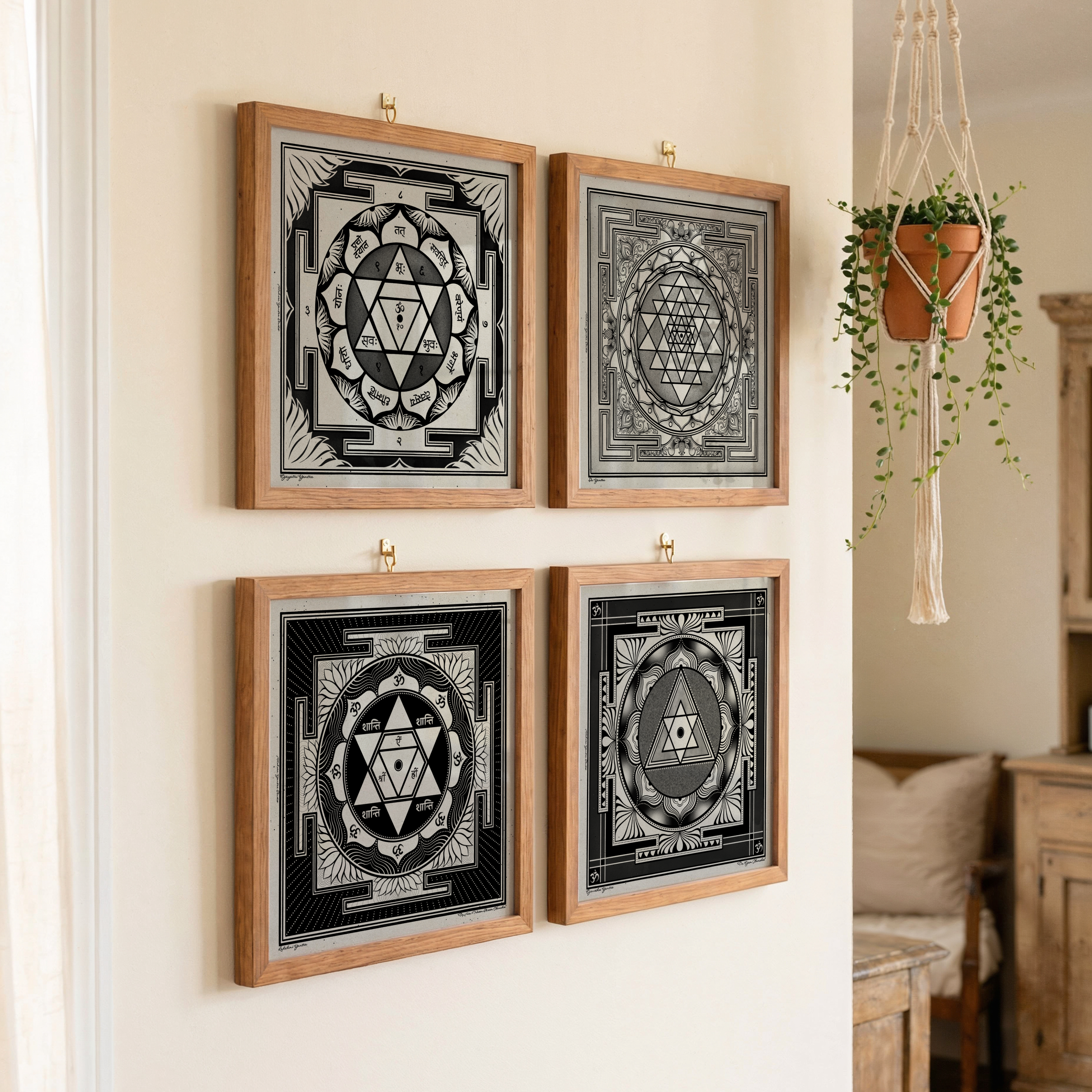 Four yantra framed black and white sacred geometric art prints featuring sacred geometry symbols, arranged in a 2x2 grid on a warm beige wall. The prints are housed in light natural wood frames and hung with small brass hooks.