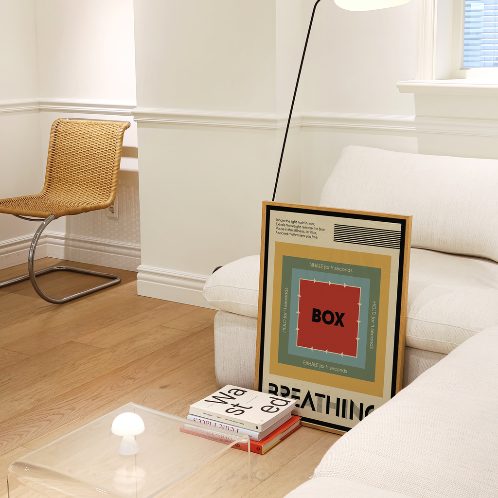 A framed art print featuring a colorful geometric design with the word 'BOX Breathing' in the center, leaning against a white sofa in a modern mid century living room setting.