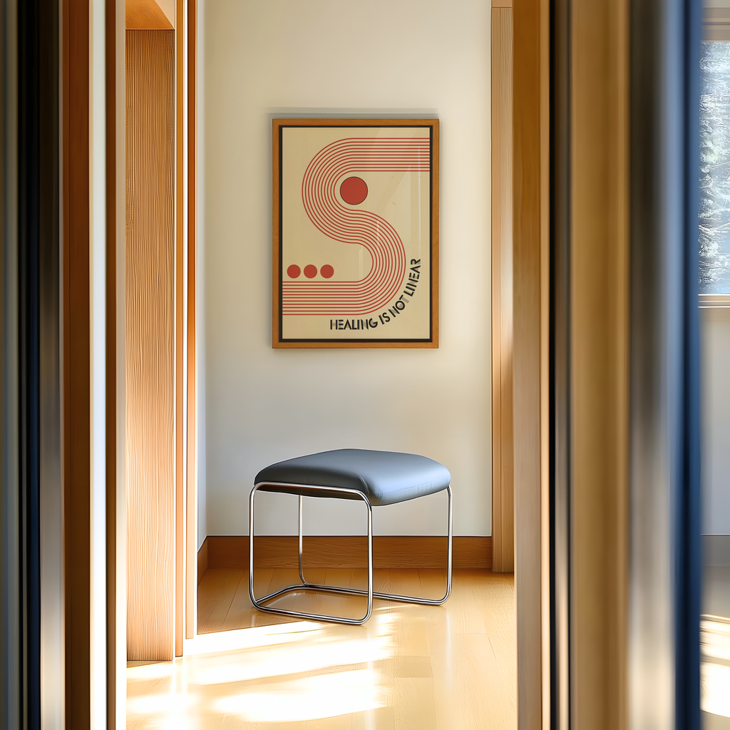 A framed Healing Is Not Linear art print hangs on a warm beige wall above a modern gray upholstered stool with a chrome frame in a bright, sunlit interior. Inspired by mid century modern and Bauhaus design, the artwork features bold geometric shapes, clean typography, and a retro color palette. This motivational print celebrates the healing journey with a timeless message, making it a meaningful addition to therapy offices, wellness spaces, home offices, or modern interiors.