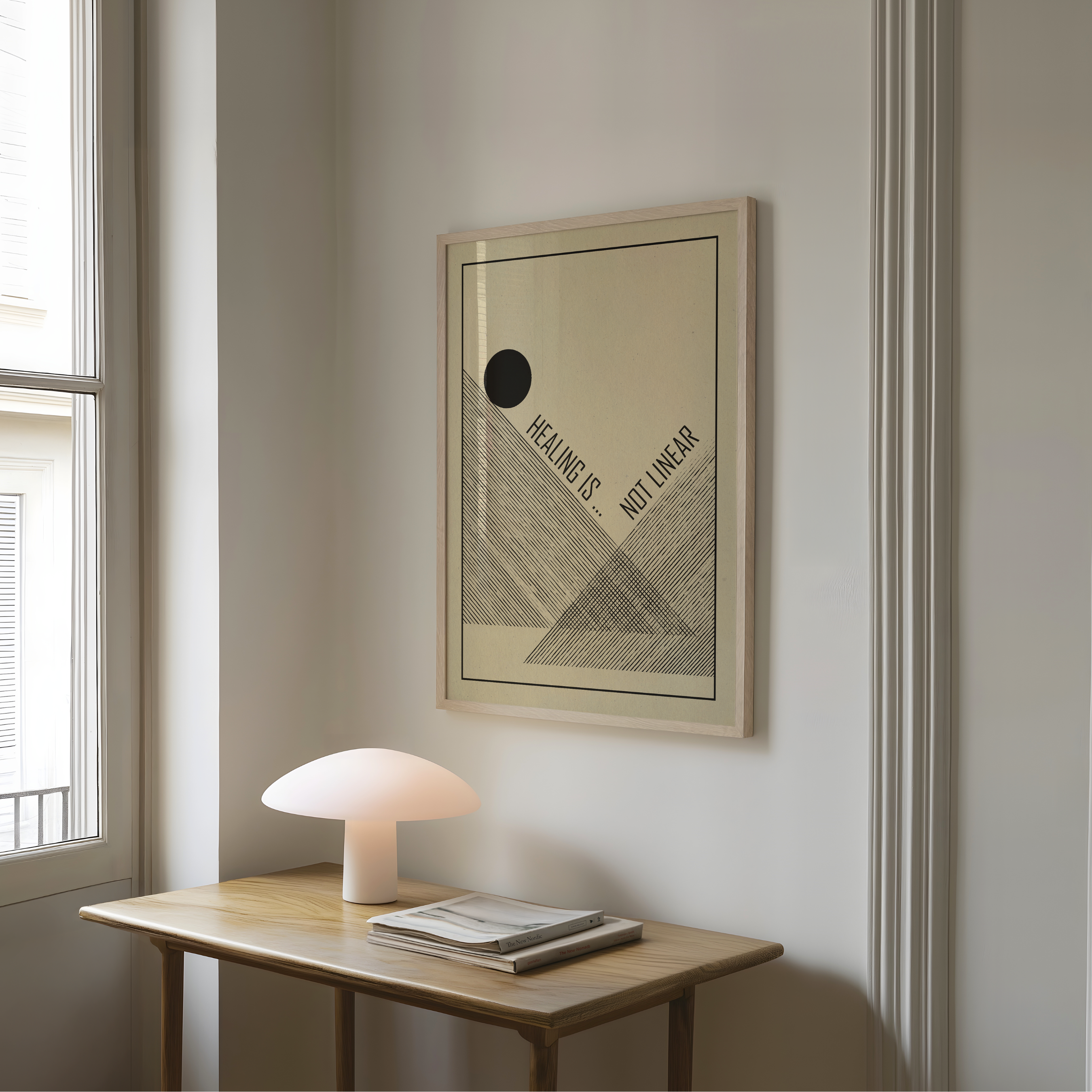 A framed Healing Is Not Linear art print featuring minimalist black geometric line art and typography on a cream background hangs on a light gray wall above a wooden table with a mushroom shaped lamp and stacked books. Inspired by mid century modern and Bauhaus design, the artwork combines clean forms and a meaningful message, offering a gentle reminder that healing is a personal journey with its own rhythm. Perfect for therapy spaces, wellness rooms, home offices, or mindful interiors.