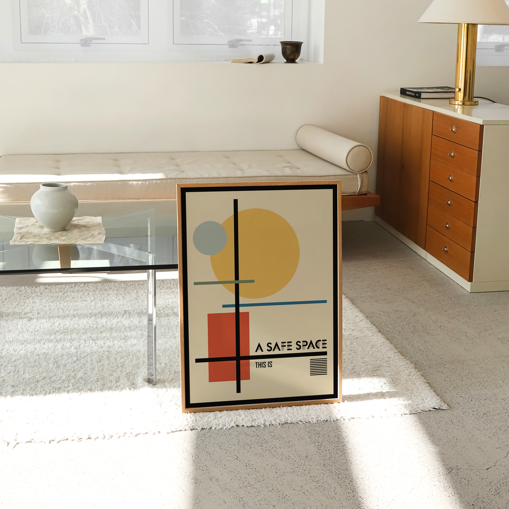 A framed Bauhaus-inspired geometric healing art print leans against a wall in a bright, modern living room. Featuring the quote "A Safe Space," this contemporary mental health wall art is ideal for therapy office decor, counseling rooms, psychologist offices, wellness clinics, and mindful home interiors.