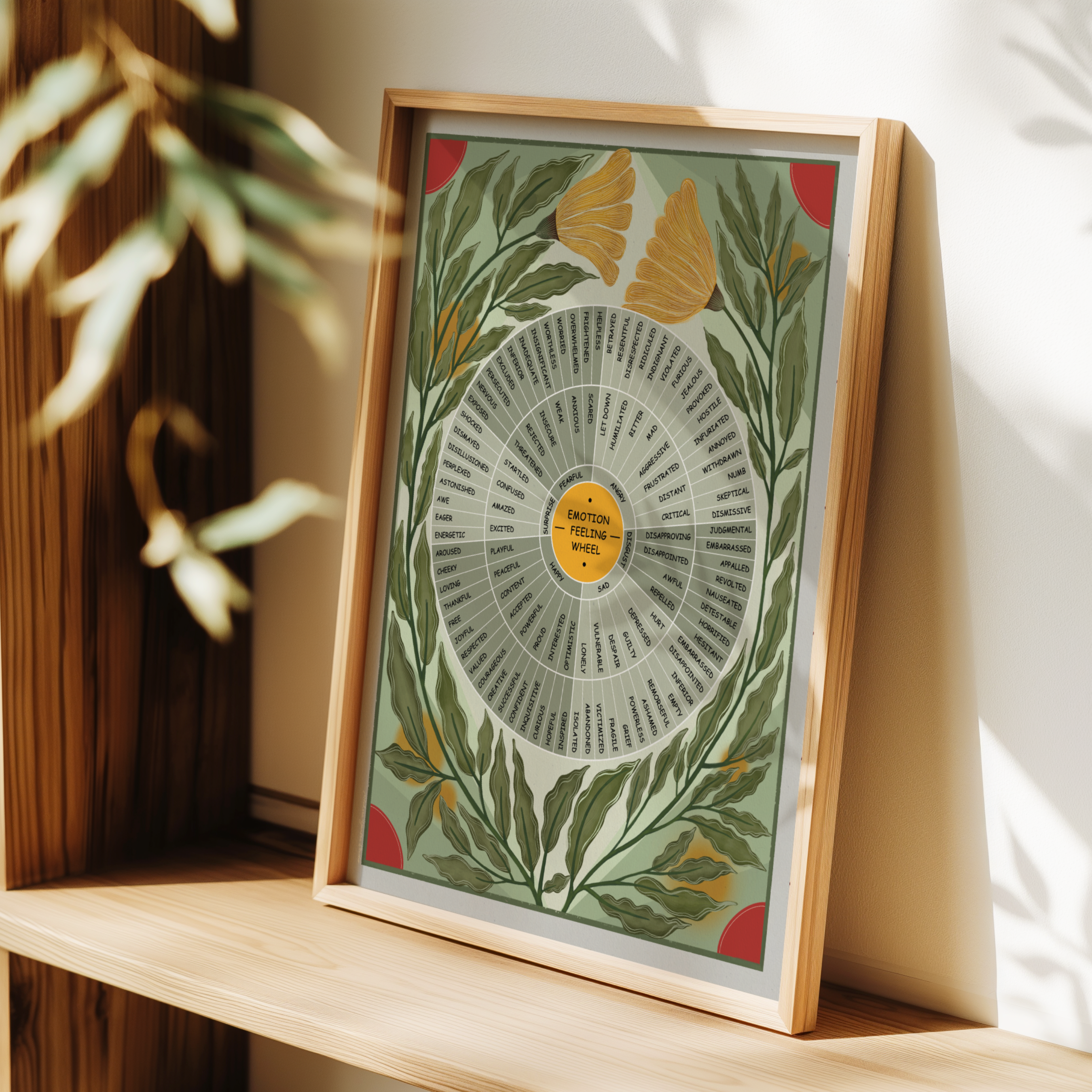 A framed botanical art print with an emotion wheel design and botanical illustrations, leaning on a wooden shelf in a warm, sunlit room.