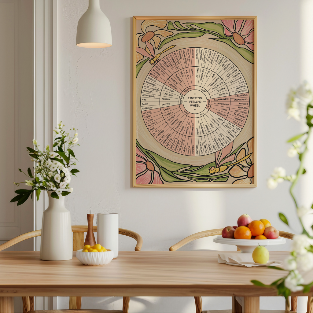 A framed vintage-style botanical emotion wheel poster hangs on a light gray wall above a wooden dining table with flowers, candles, and fruit in a softly lit interior.