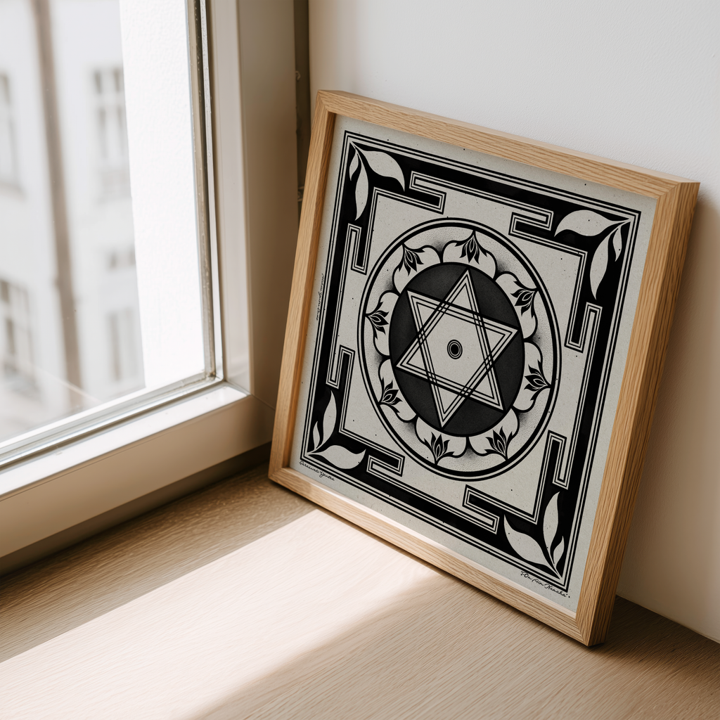 A square framed art print featuring a black and white geometric Saraswati yantra, leaning against a wall on a windowsill in a sunlit room.