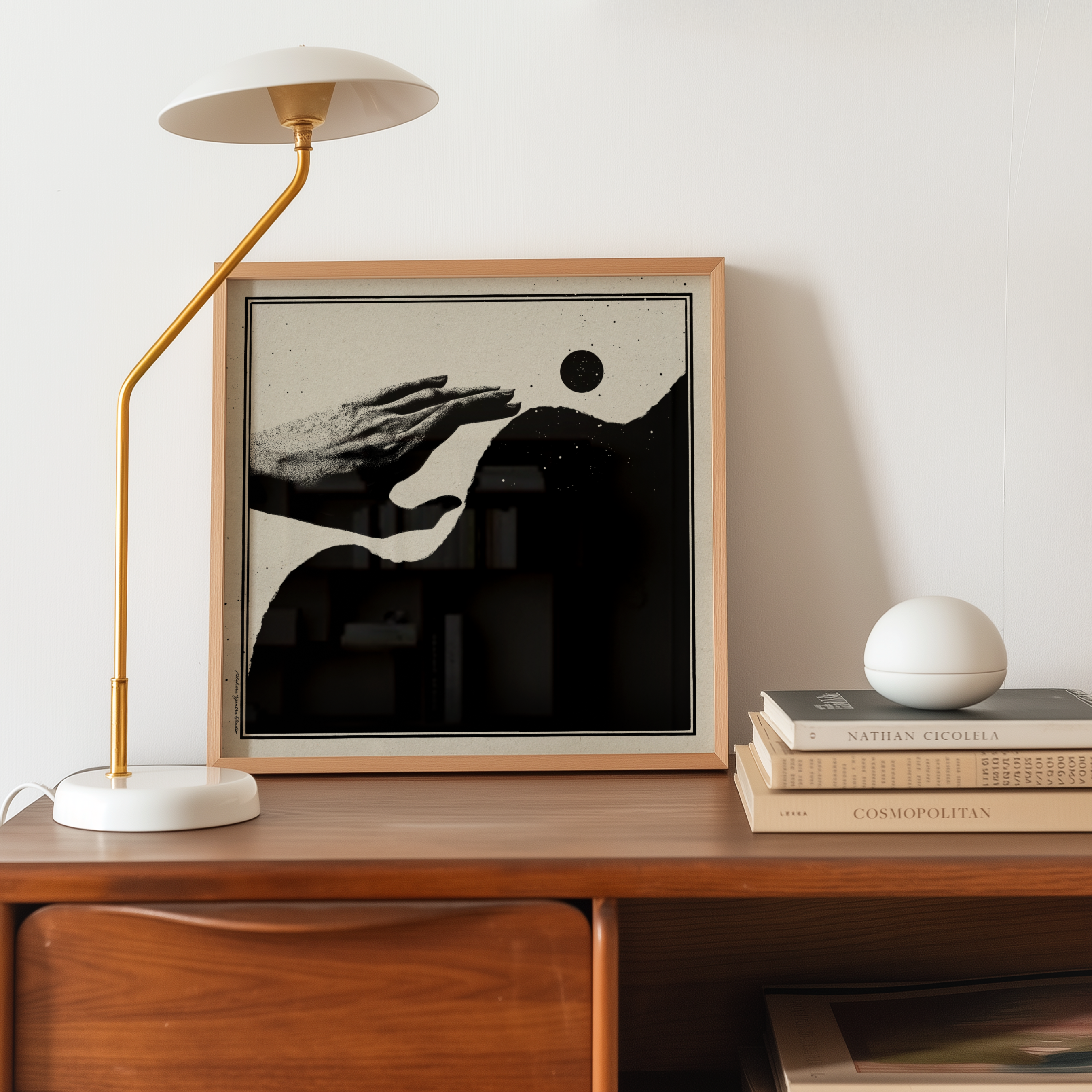 A framed Momentum abstract healing art print featuring a minimalist black and beige illustration of an outstretched hand, organic forms, and a black moon. Styled on a wooden console table beside a gold and white table lamp and a decorative white sphere, this motivational wall art brings solace, resilience, and calm to modern, Scandinavian, Japandi, and contemporary home decor.