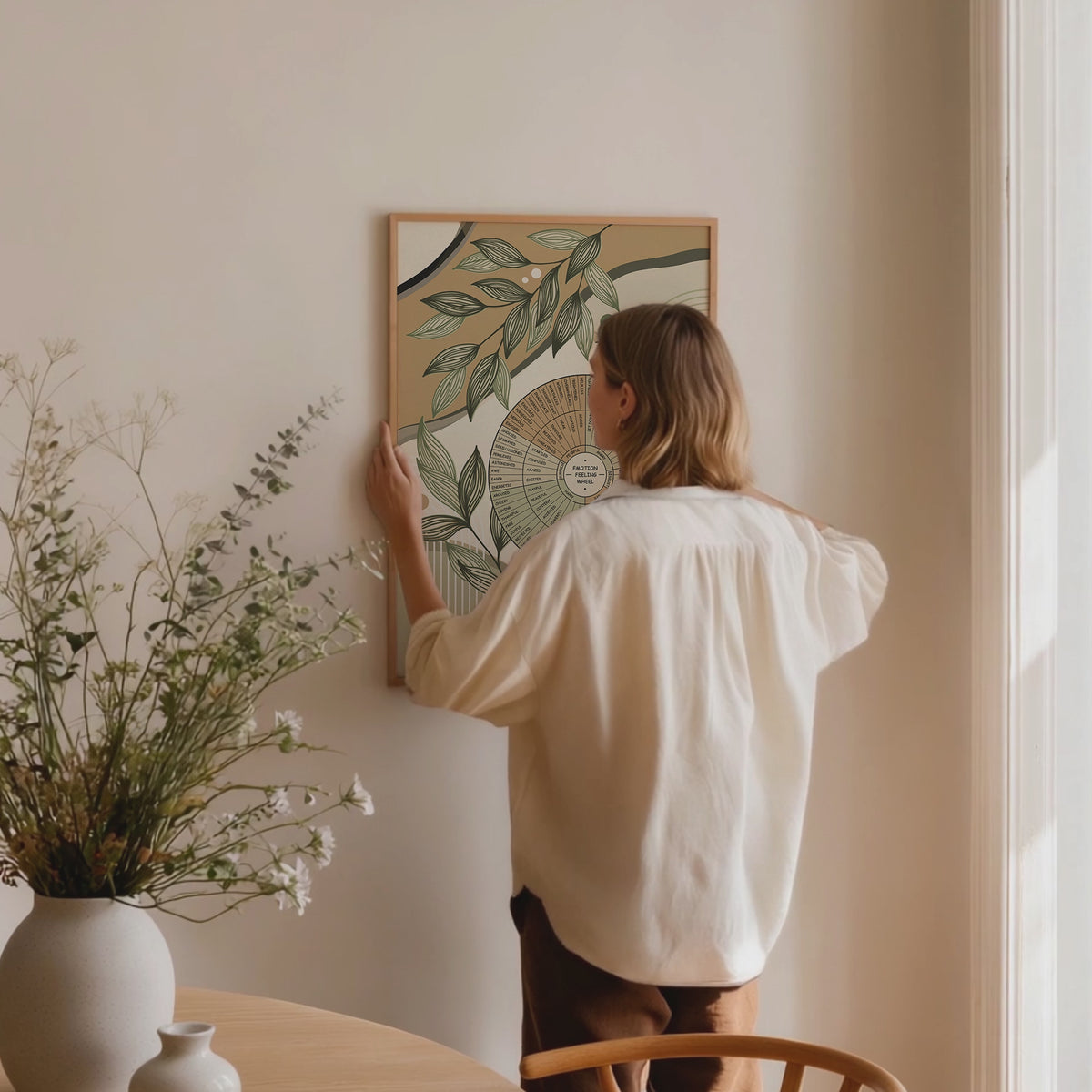 Video of the emotion wheel framed poster is being hanged by a woman in a peaceful room with natural light.